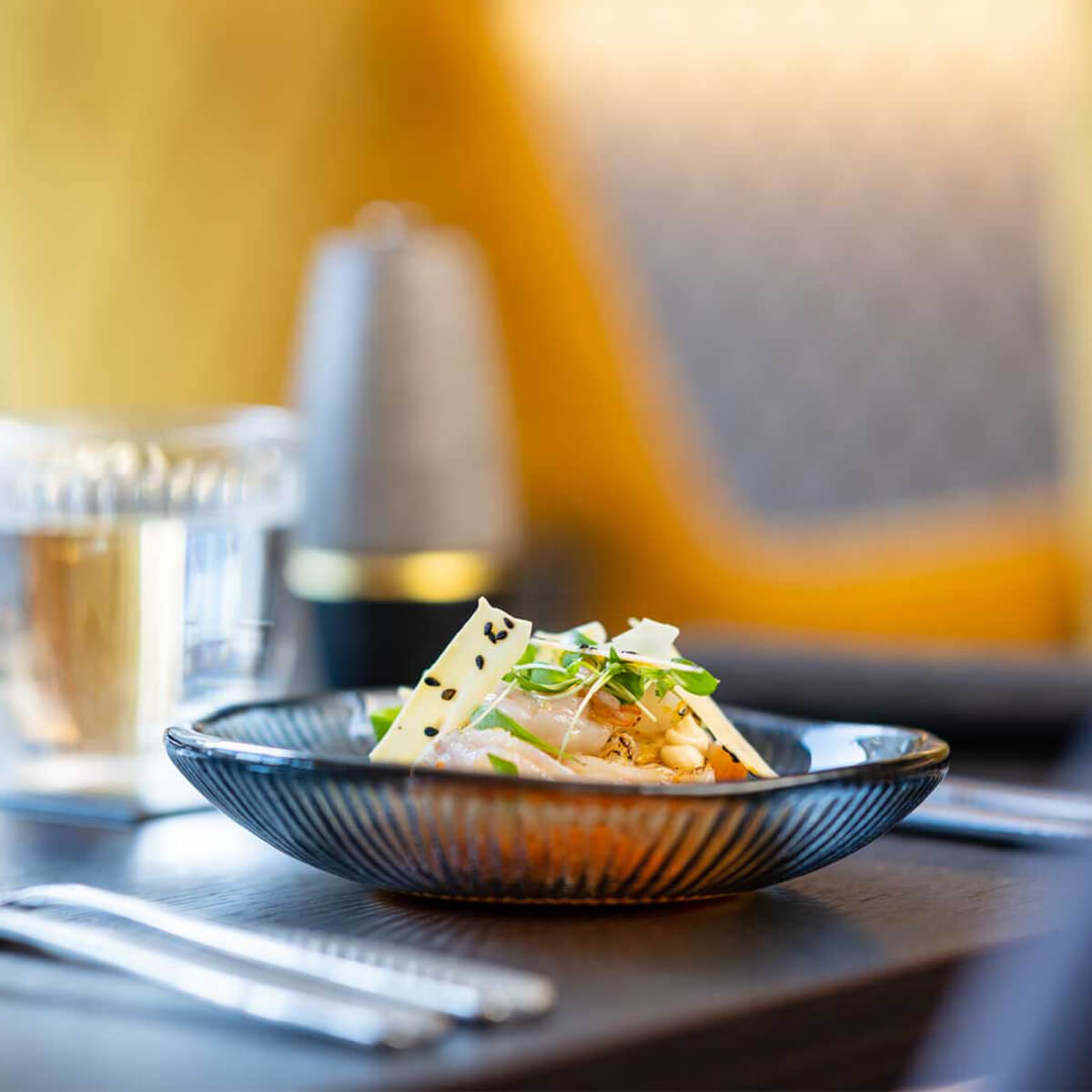 A delicate plated fish dish against warm mustard-velvet seating at The Tollhouse