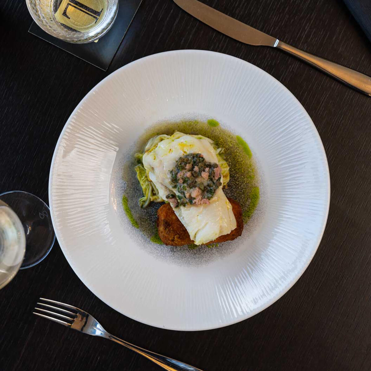 Roast cod over hispi cabbage with caper and brown-shrimp butter and a potato croquette, viewed from above